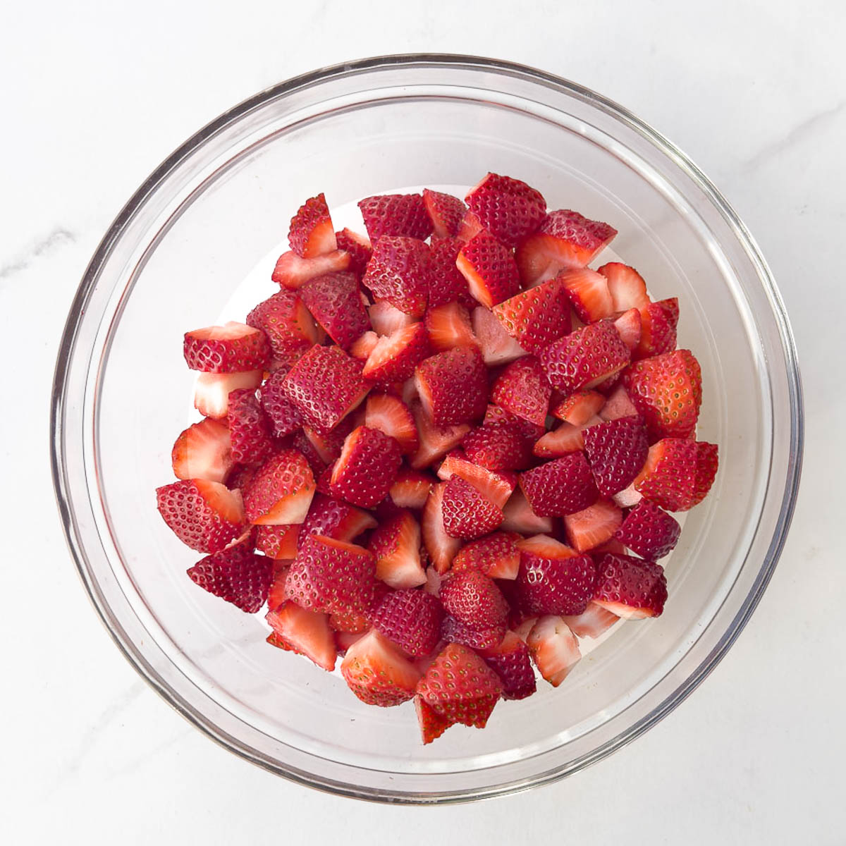  A glass bowl filled with chopped red strawberries.
