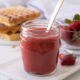 Bright red strawberry coulis (strawberry sauce), in a jar with a gold spoon.