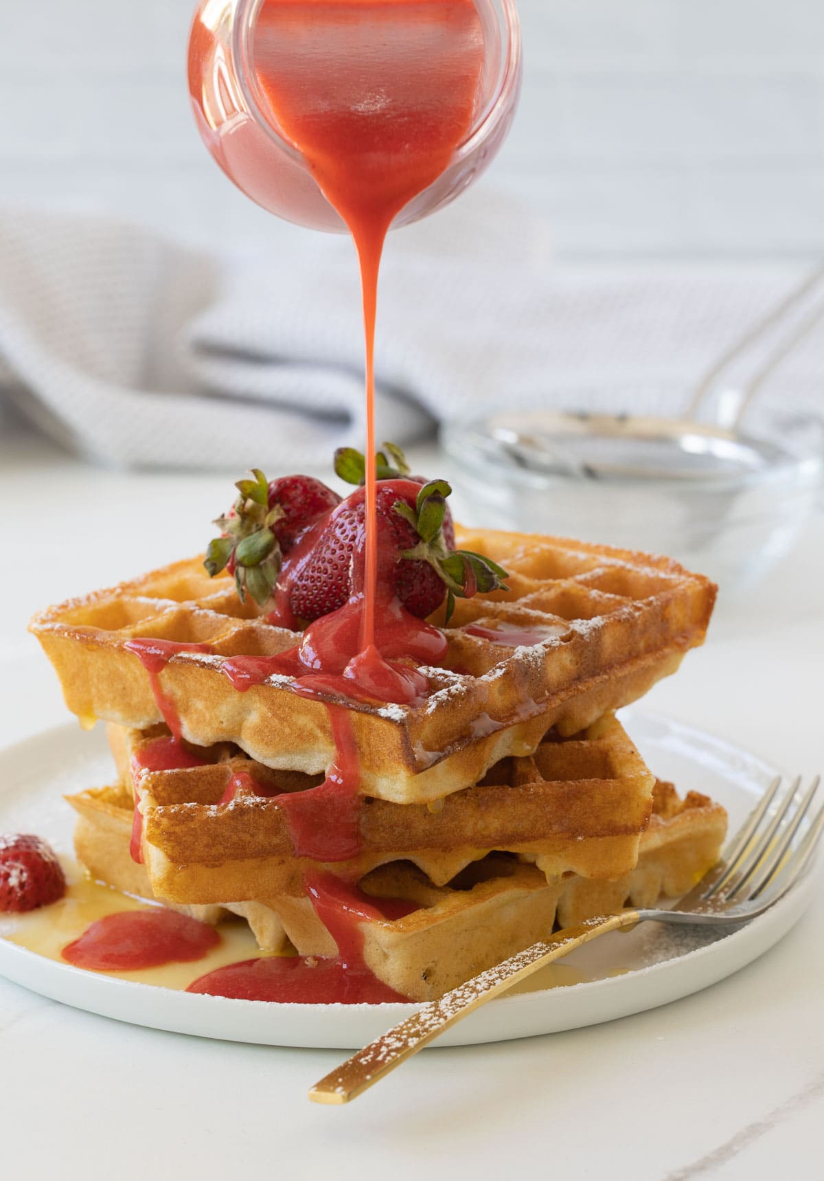 Golden gluten-free waffles with melted butter and strawberry sauce poured over the top.