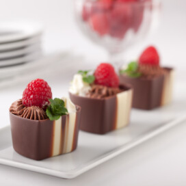 Easy chocolate mousse piped into chocolate cpus with raspberries on top.