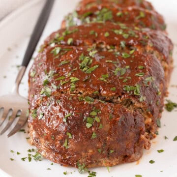 Bbq glazed beef meatloaf on a platter with a serving fork, sprinkled with chopped parsley.