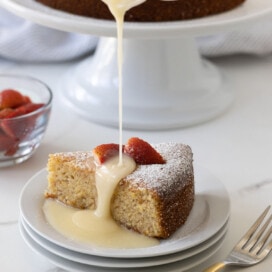 A golden slice of lemon olive oil cake, made wit whole almonds, served with berries and glaze.