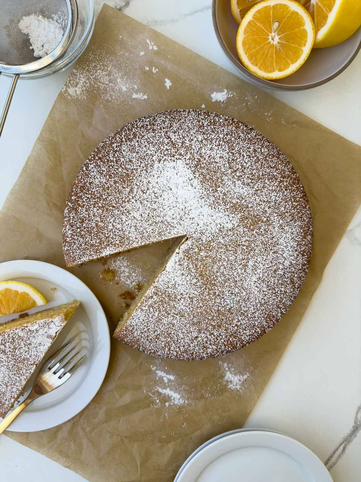 Top down view of a baked olive oil cake sifted with powdered sugar on parchment paper.
