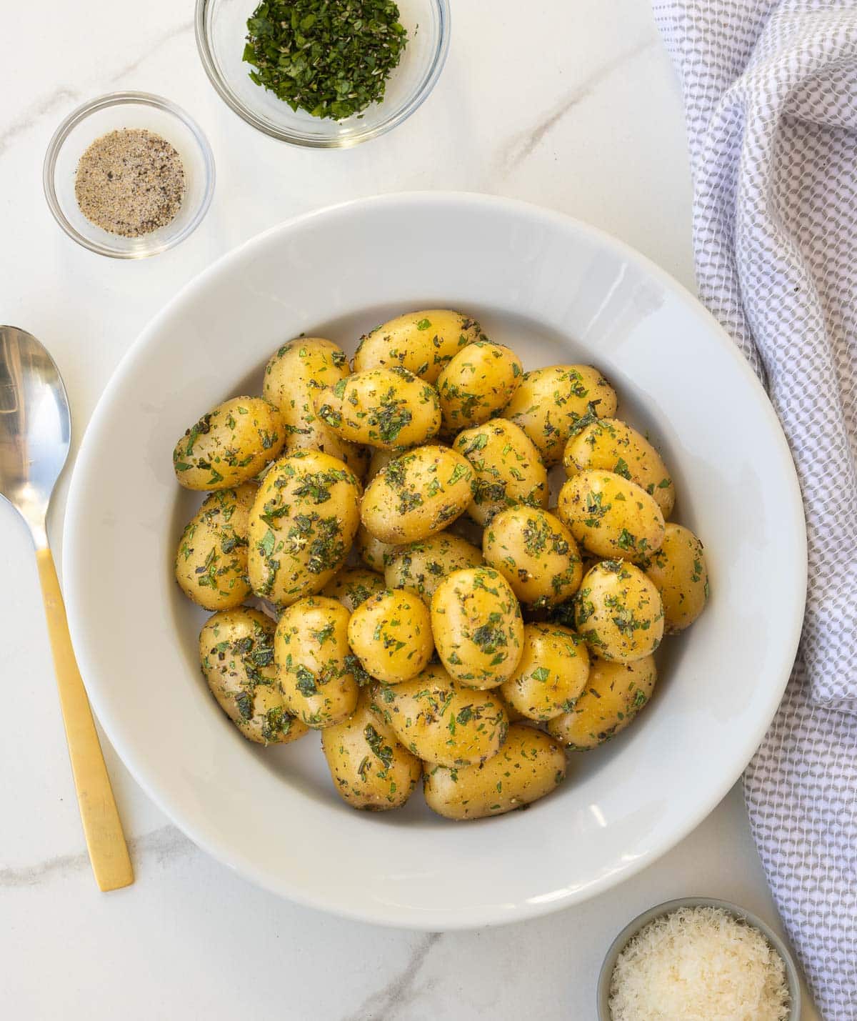 Herbed baby potatoes in a white bowl at the table for serving.