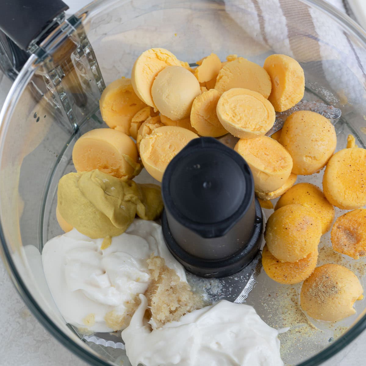 Ingredients for deviled egg filling in the workbowl of a food processor.