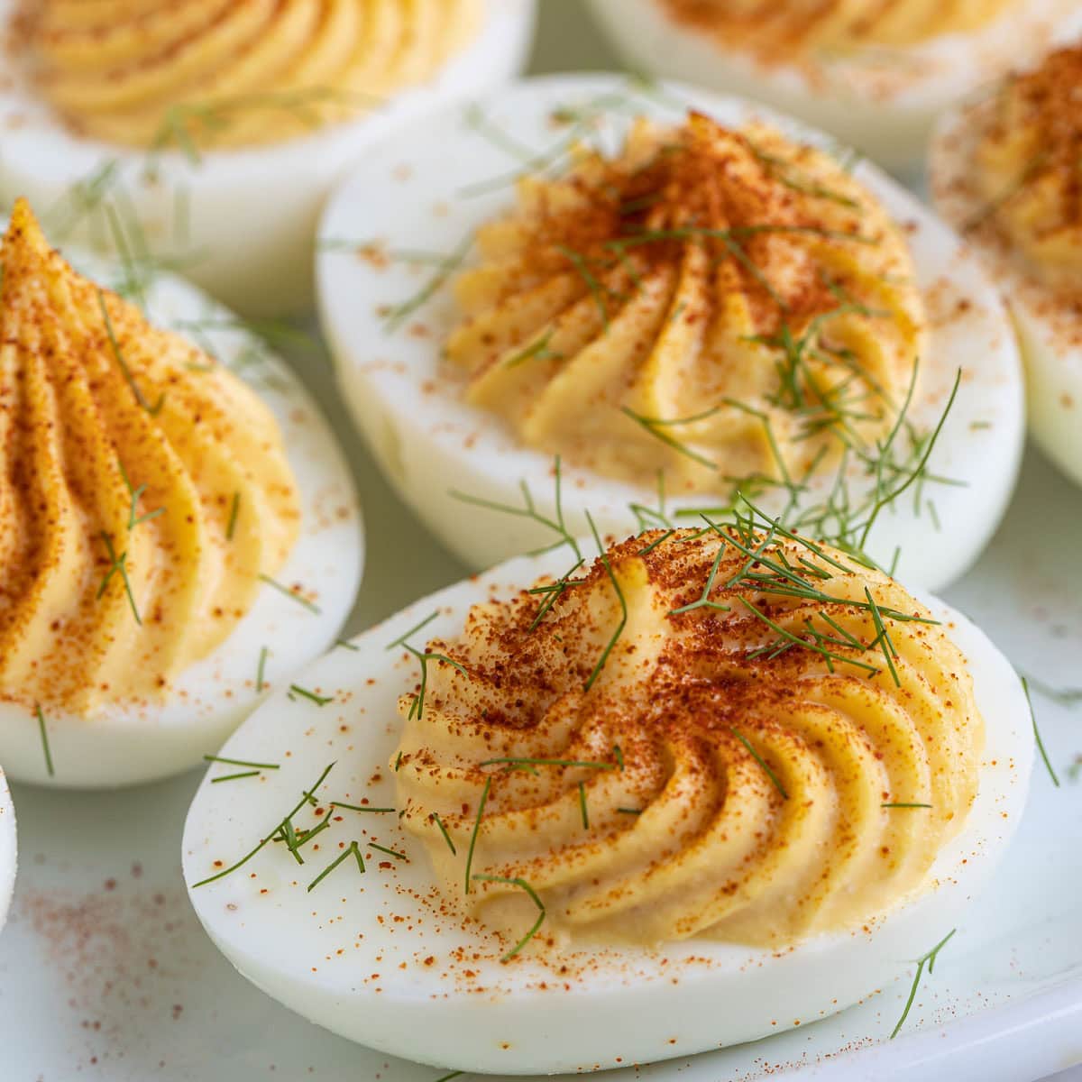 Deviled eggs garnished iwht red paprika and a sprinkle of herbs.