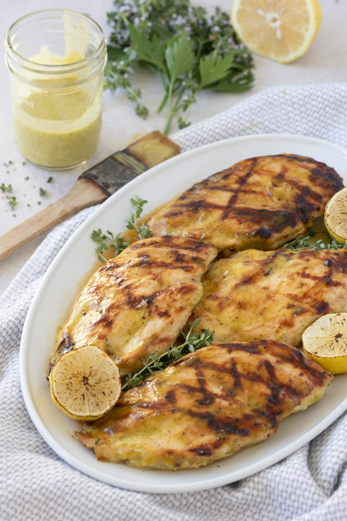 White platter of grilled chicken breasts with lemon and herbs.