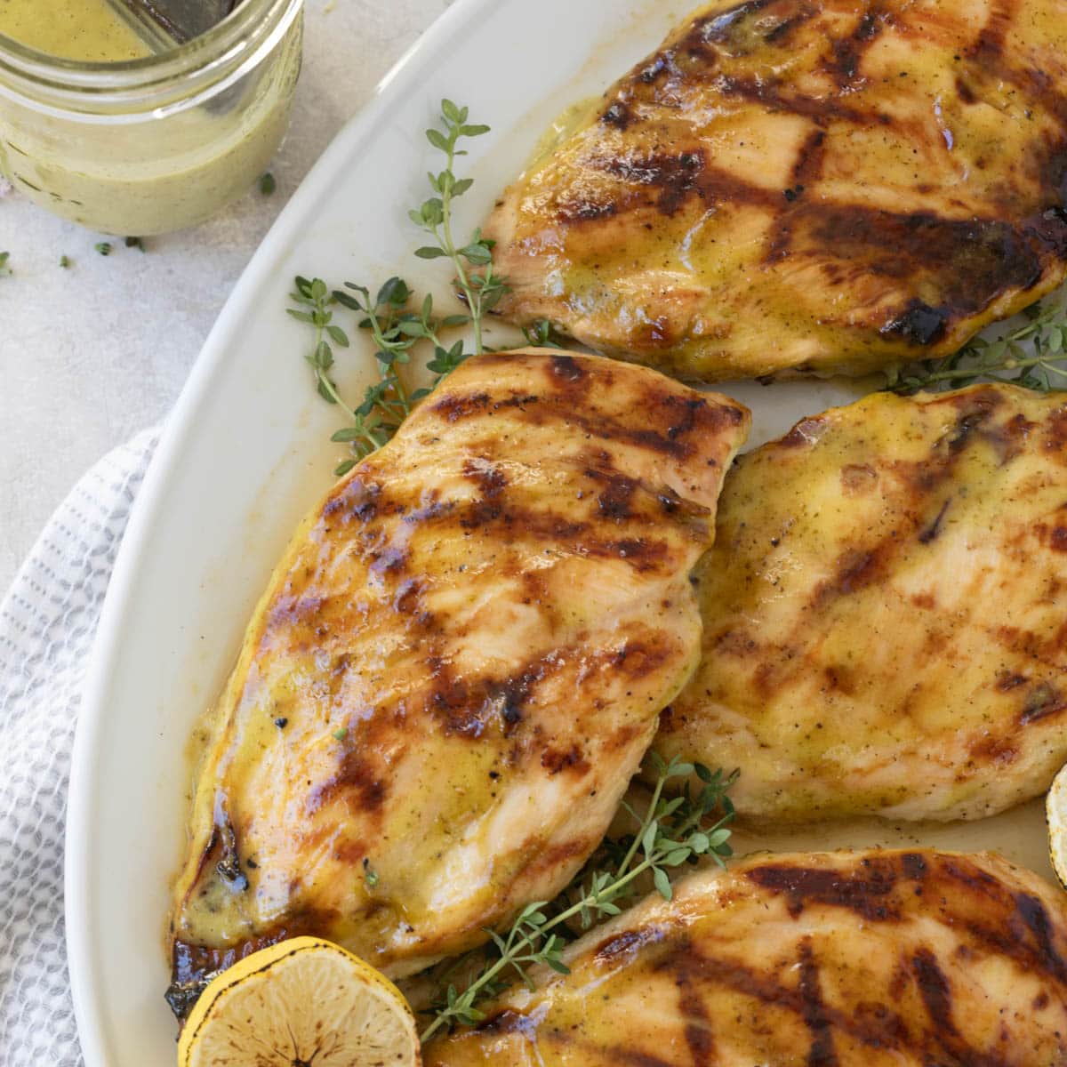 Platter of grilled chicken breasts with herbs and grilled lemon halves.