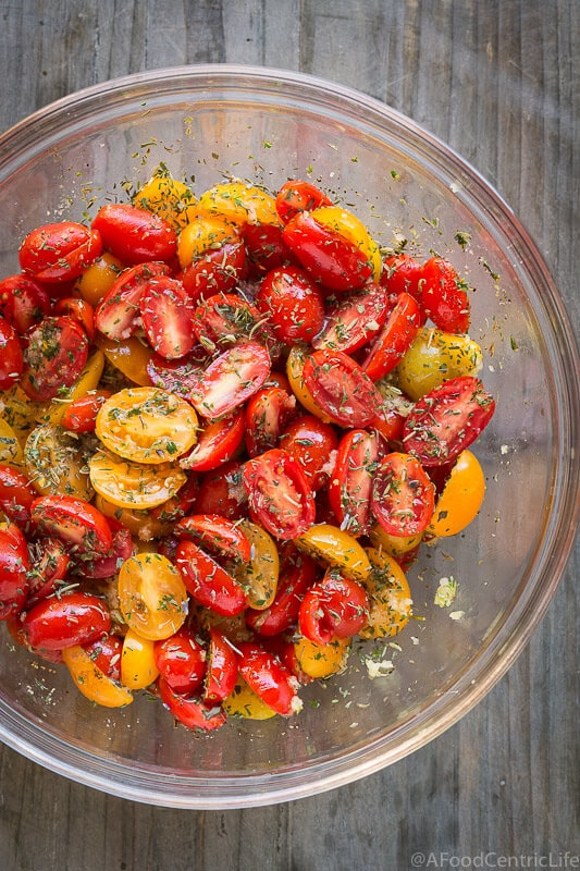 Halved fresh tomatoes in a glass bowl with oil and herbs.