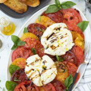 Plate of red, yellow and burgundy tomatoes with burrata and basil.