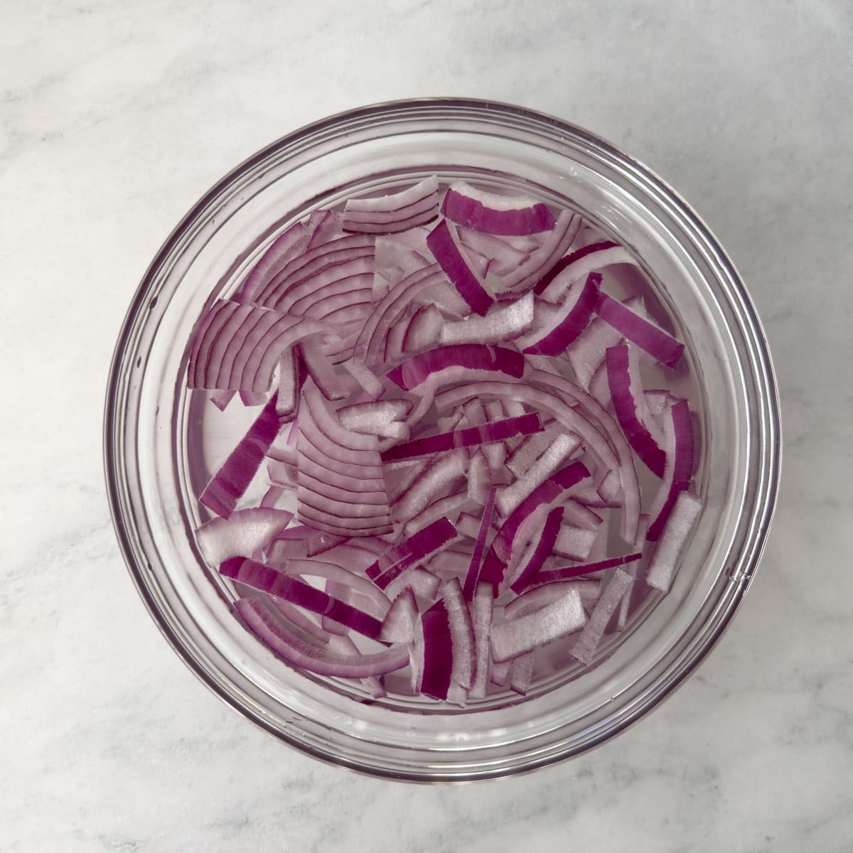Soaking thinly sliced red onions in cold water to reduce their pungency.