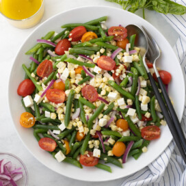 Cold green bean salad with cherry tomatoes, corn, feta and red onion in a white bowl.