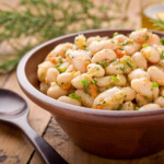 A simple white bean salad in a wooden bowl with bits of lemon zest, herbs, and carrots and a serving spoon near.