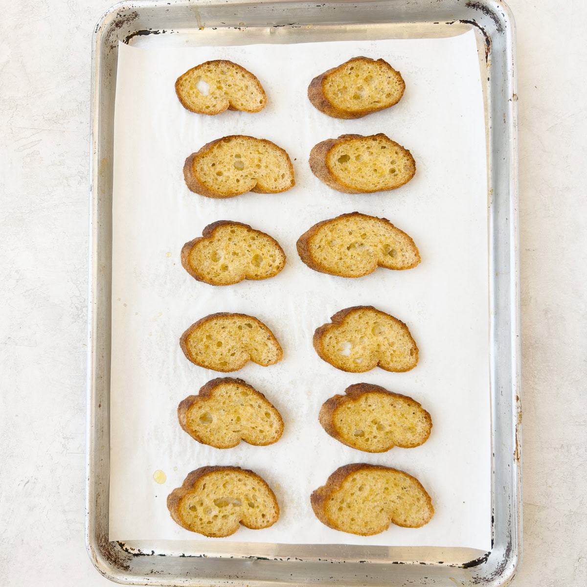 Golden baked crostini on a parchment covered baking sheet.