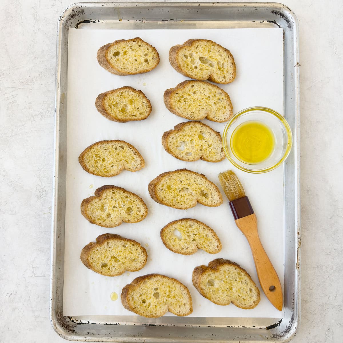 Baguette slices brushed with olive oil with a pastry brush.