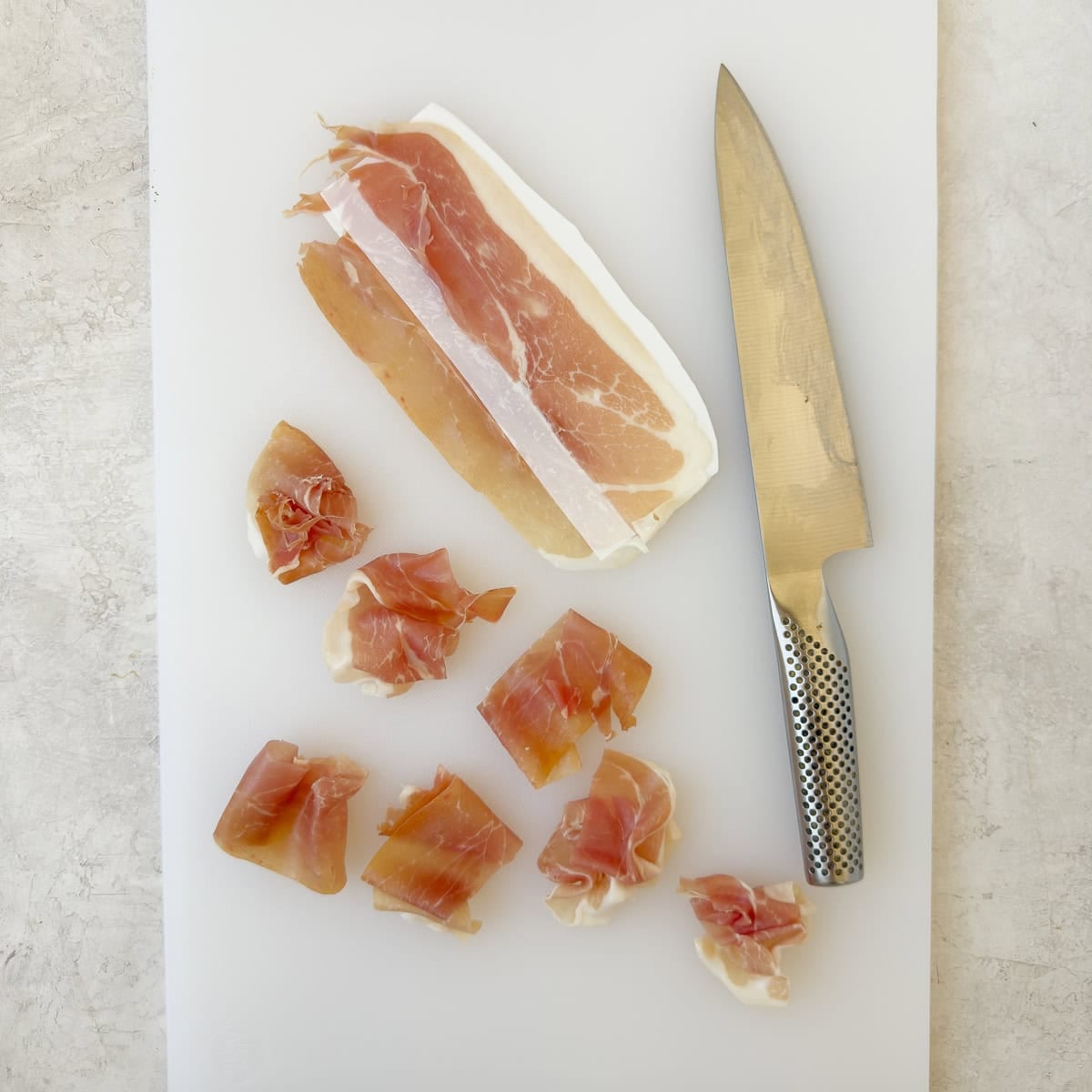 Slicing prosciutto pieces in half to make goat cheese crostini.