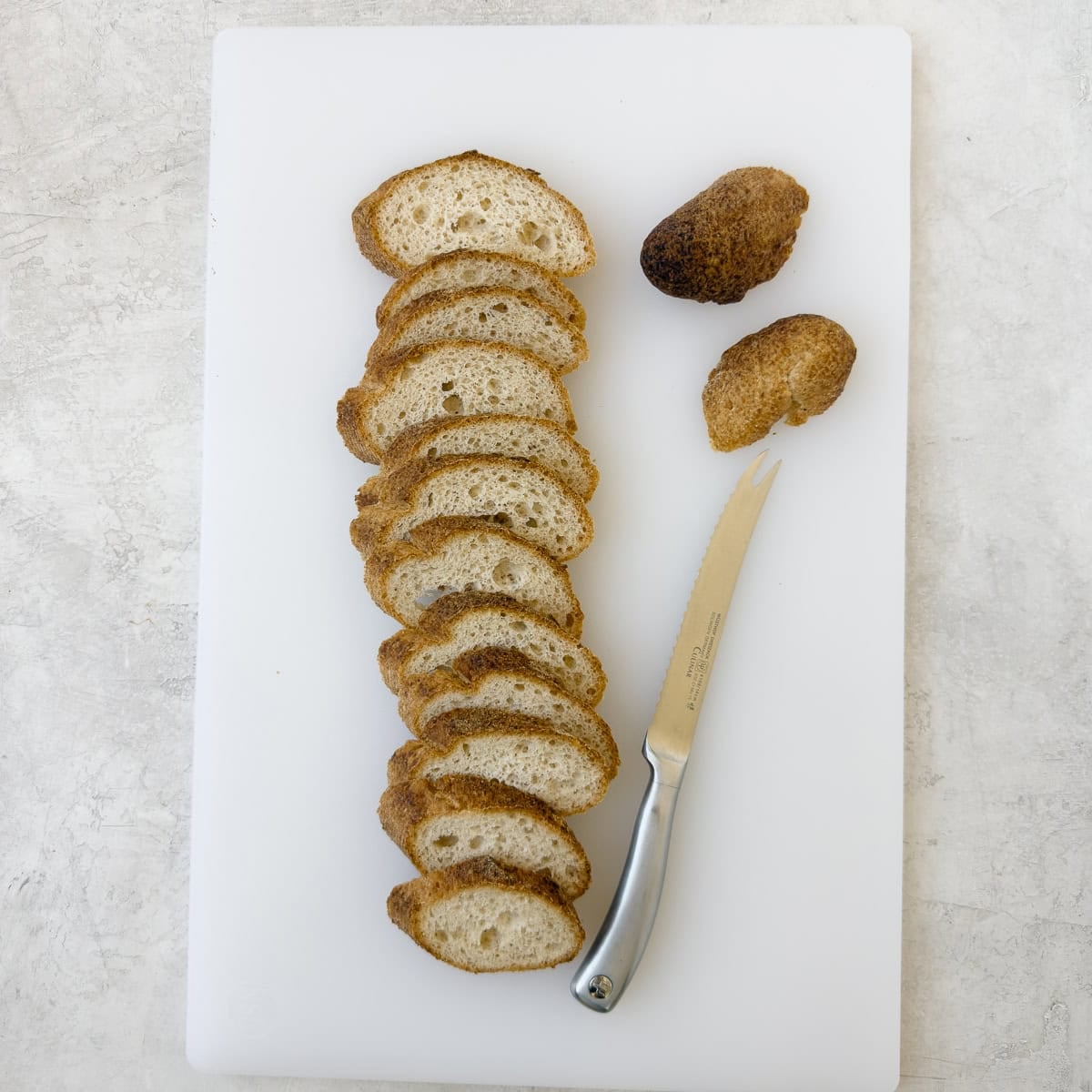 Sliced baguette on a white cutting board with a serrated knife.