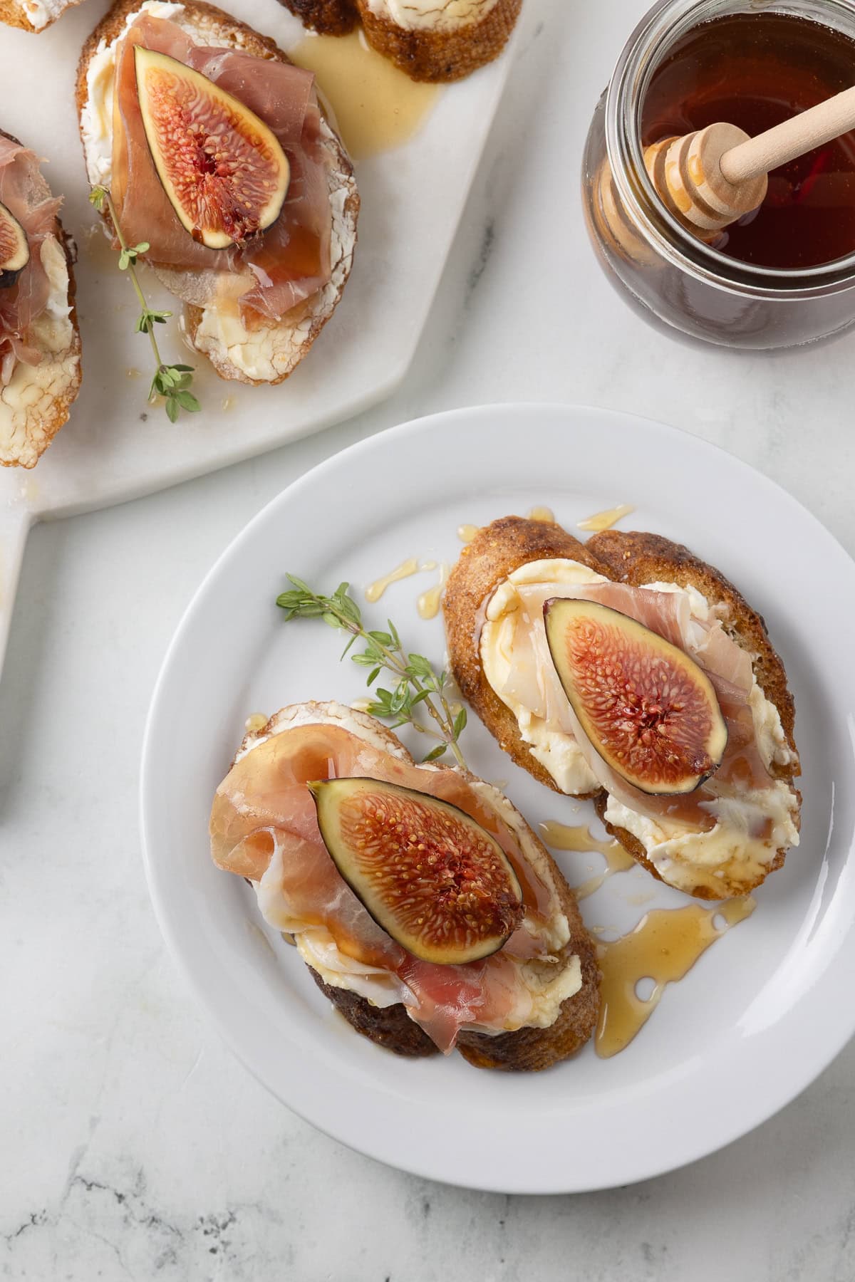 Two goat cheese crostini with figs and prosciutto on a small plate with platter beside.