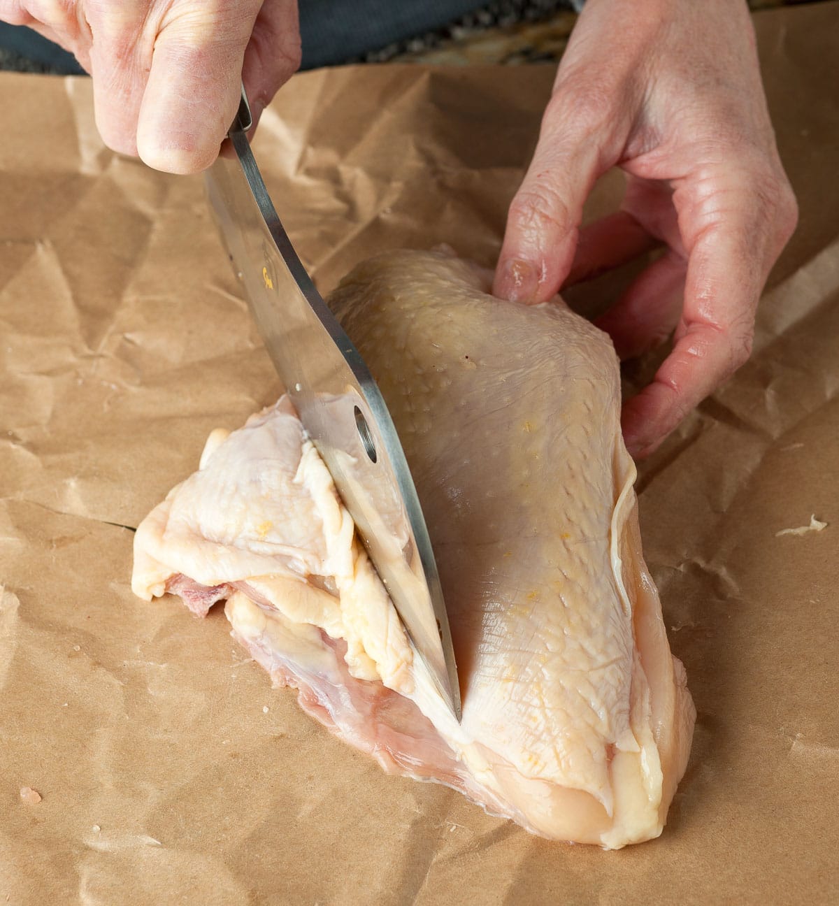 Trimming small ribs bones from a raw bone-in chicken breast.