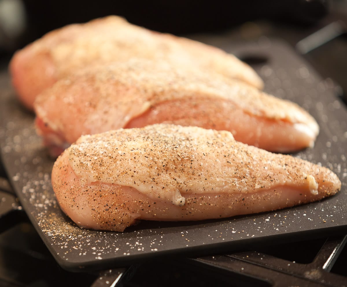 Seasoned raw chicken breast on a black cutting board.