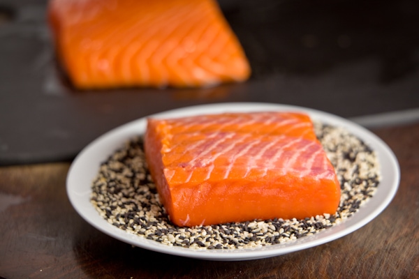 Bright orange raw salmon on a plate fo black and white sesame seeds.