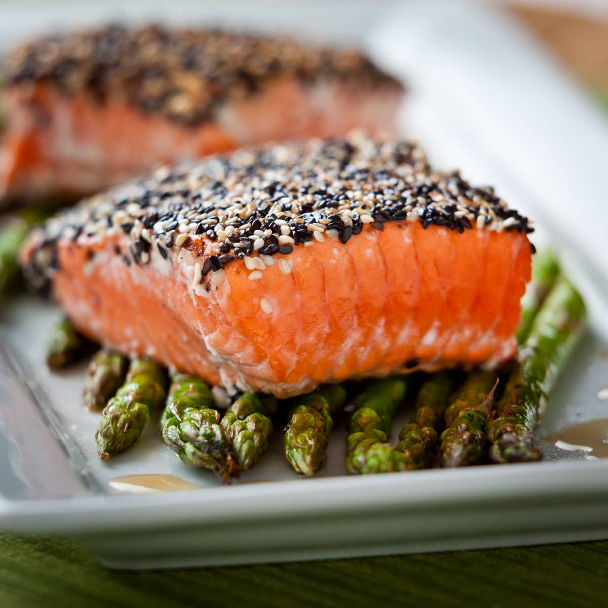 Closeup of a salmon filet with a black and white sesame crust on asparagus spears. 