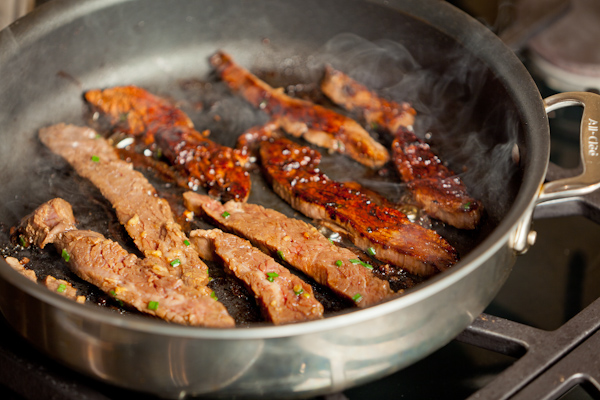 Flank steak cooking in pan.