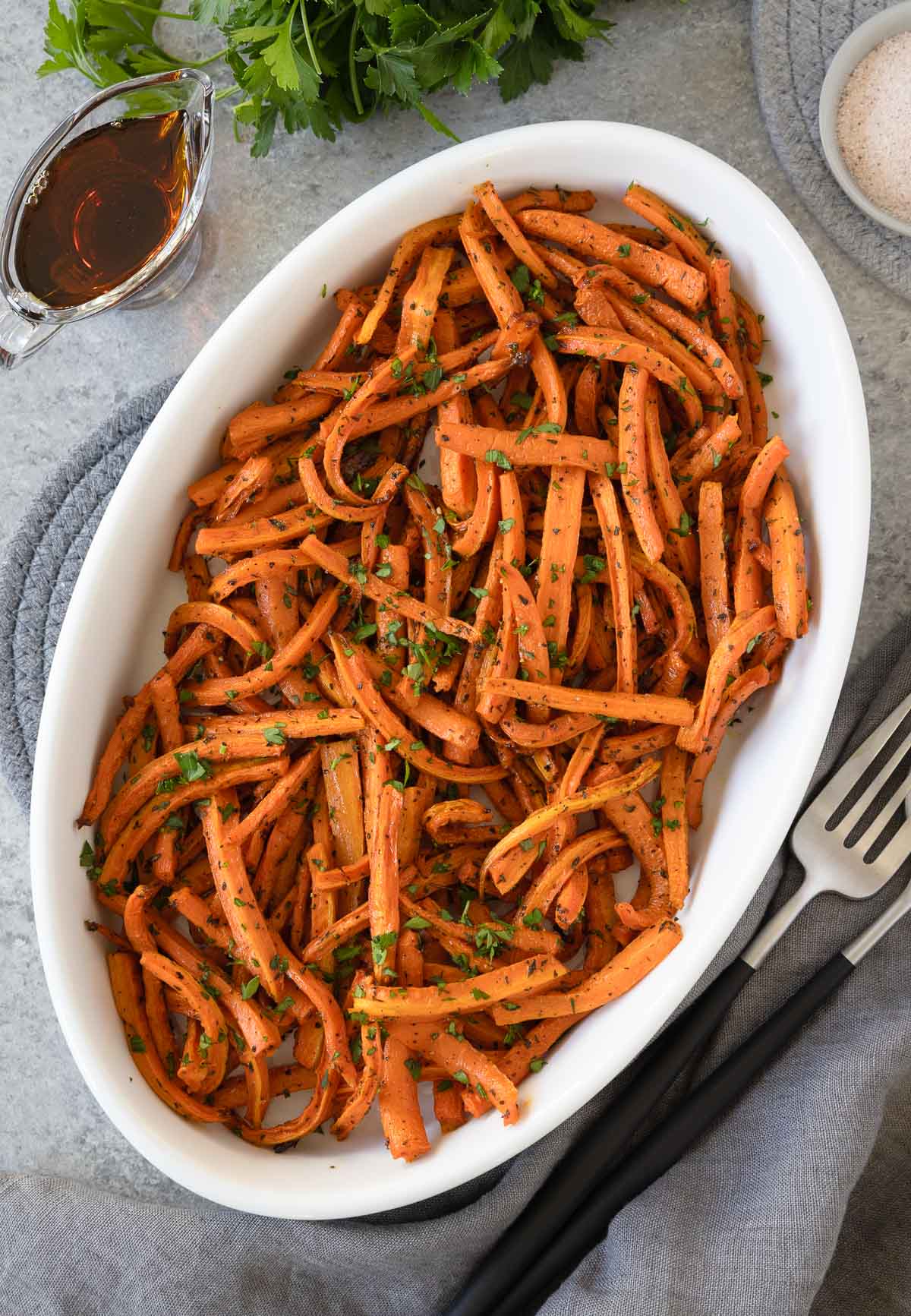 an oval dish of maple roasted carrots with herbs, maple syrup by the side.