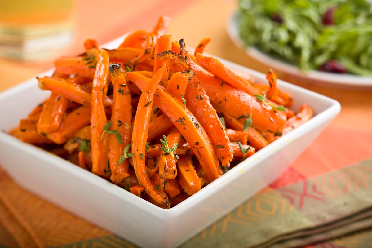 Roasted carrots in a white bowl on the table with fresh green thyme.
