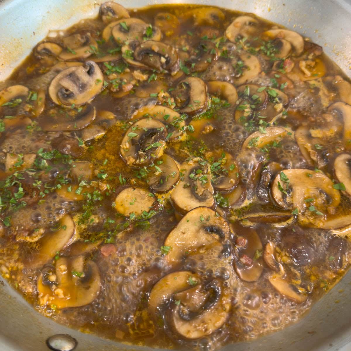 Bubbling mushroom in a pan with fresh green herbs and butter for chicken marsala.