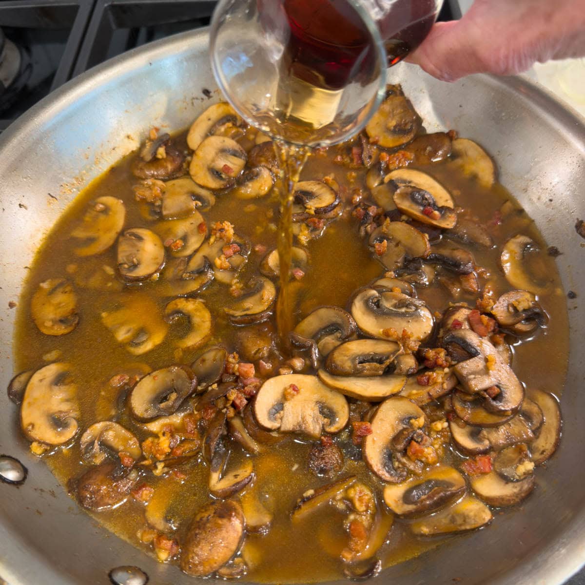 Marsala wine pouring into a pan with mushrooms for chicken marsala sauce.