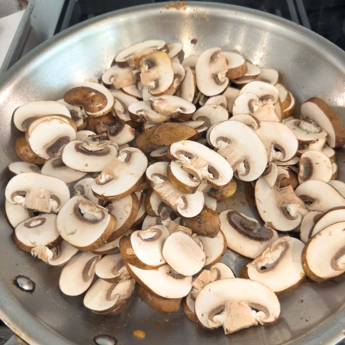 Sliced cremini mushrooms in a fry pan for cooking.