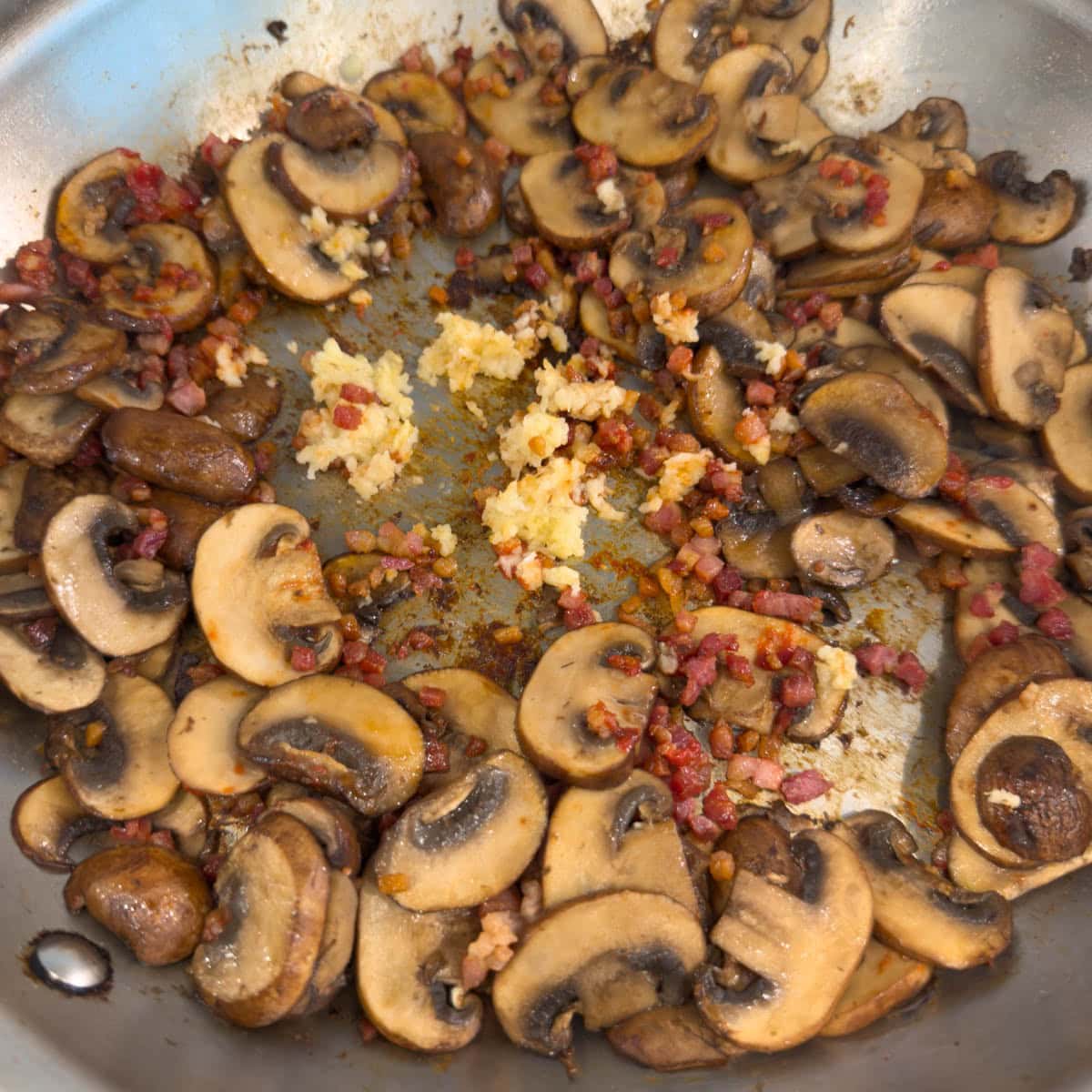 Sautéed mushrooms with cooked pancetta and garlic in a skillet.