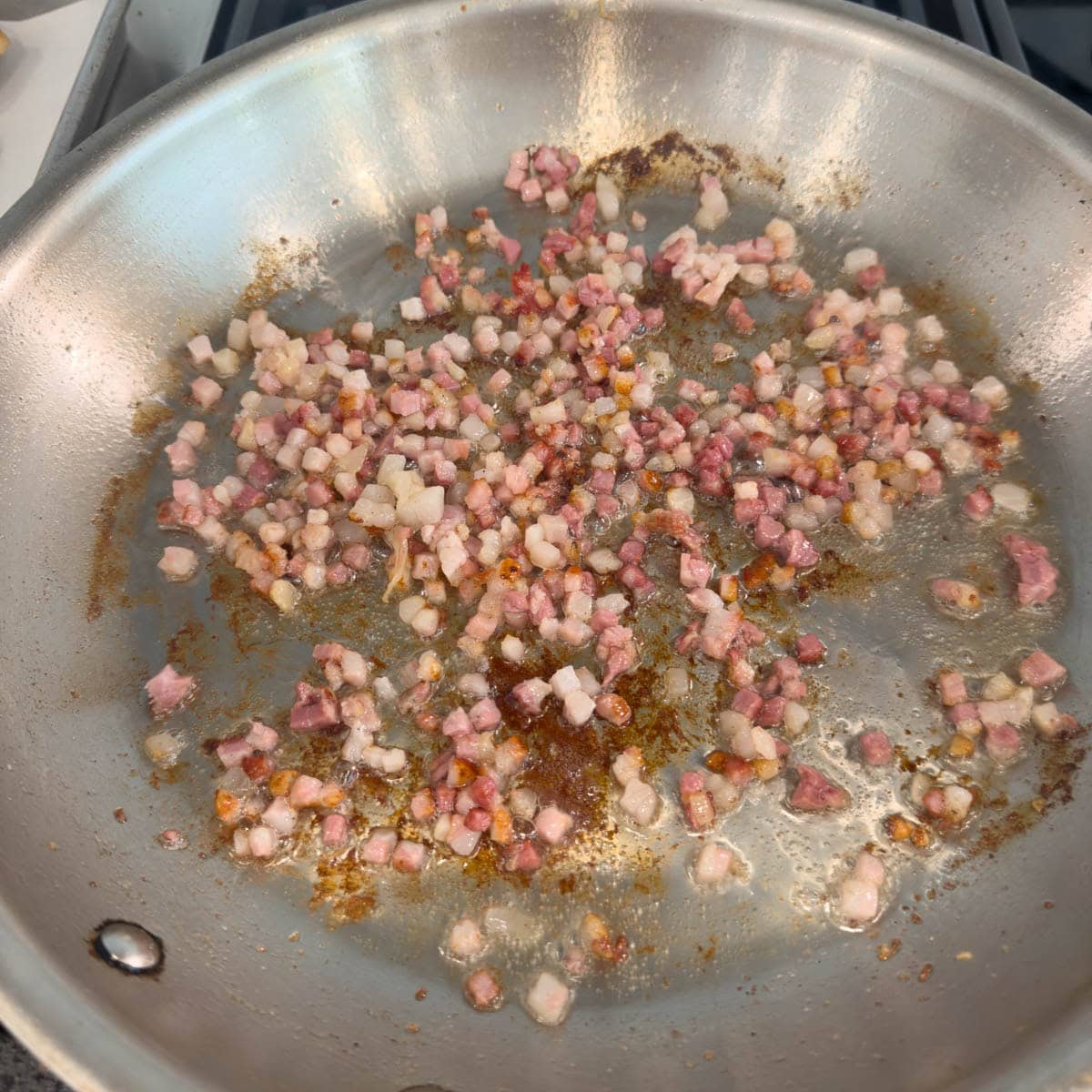 Cooking diced pancetta in a stainless skillet.