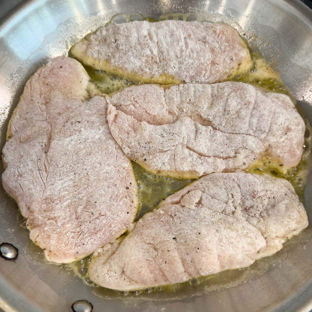 Floured chicken breasts sauteing in olive oil and butter in a fry pan.