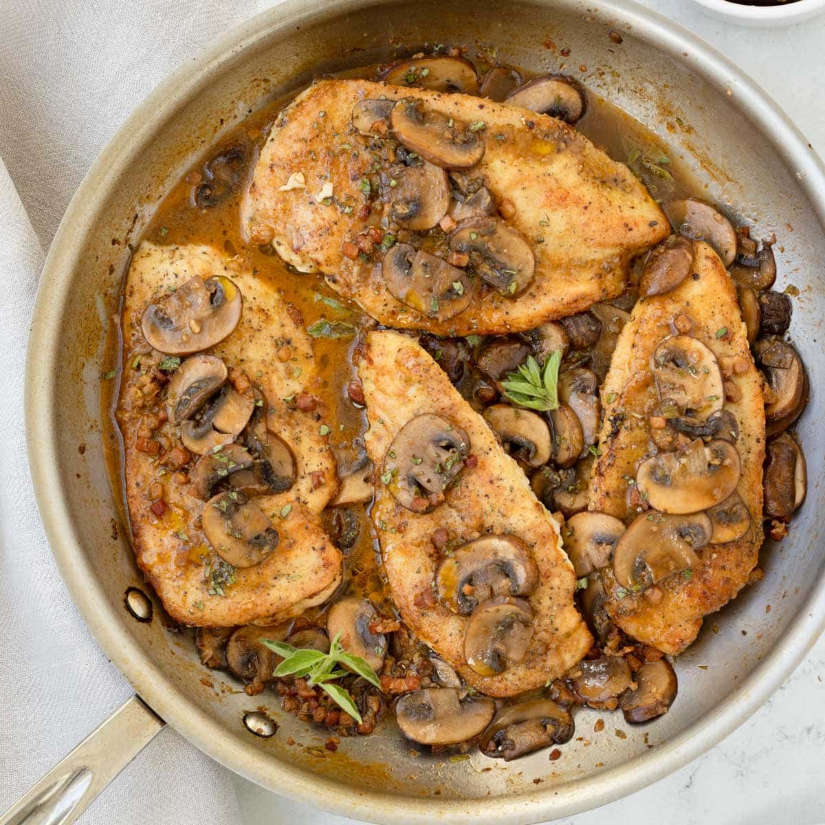 A saute pan of Chicken Marsala without cream, topped with mushroom sauce and herbs.