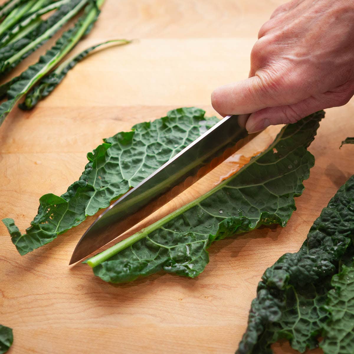 Slicing the tough center ribs from kale leaves on a cutting board.