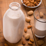 A glass dairy bottle of homemade almond milk with raw almonds on a wooden table.