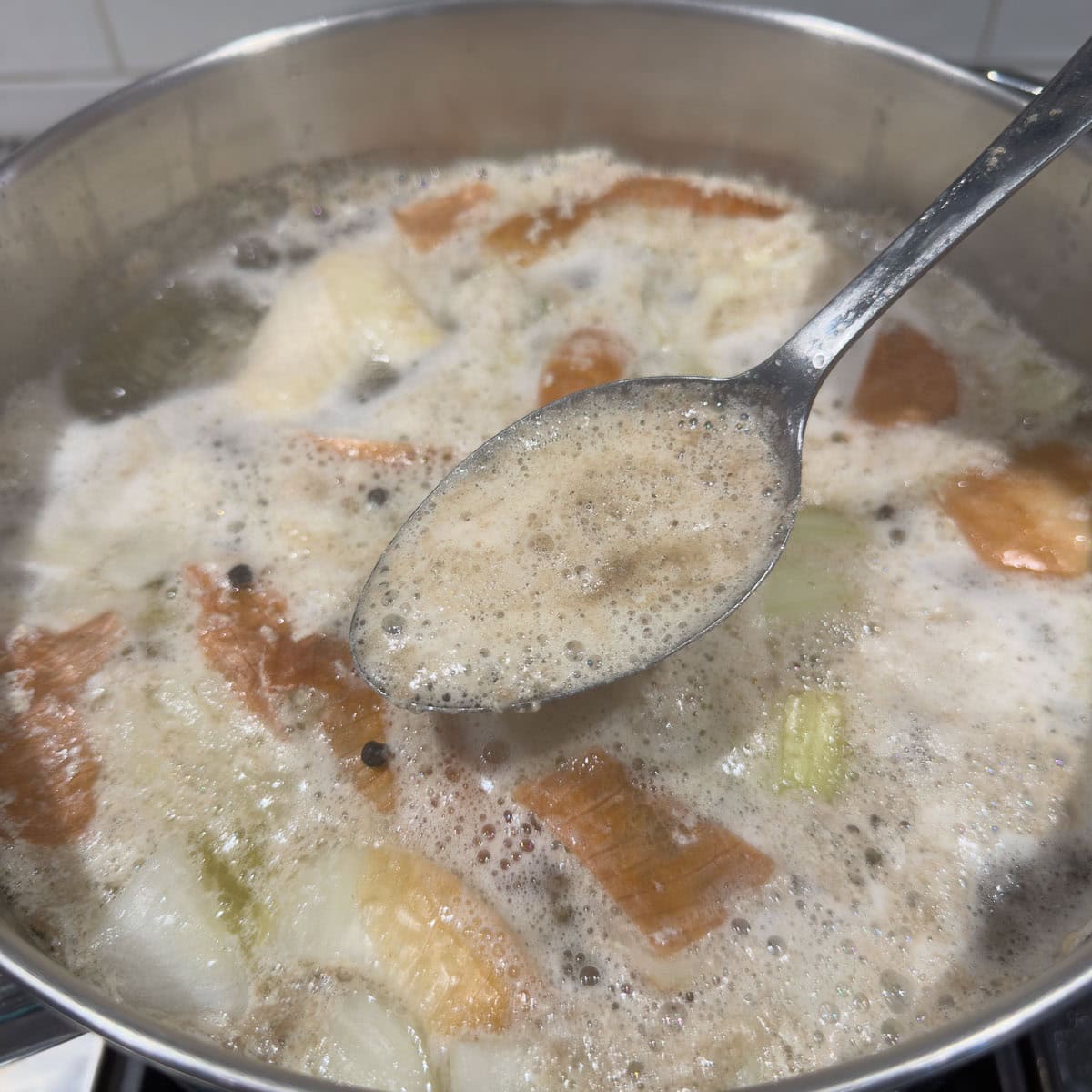 Skimming impurities from chicken broth while it is simmering.