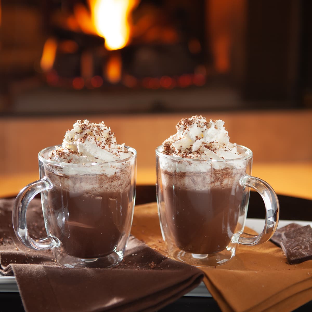 Hot chocolate with whipped cream topping in front of a fireplace.