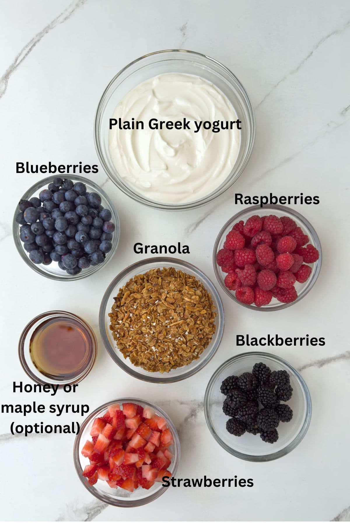 Ingredients for yogurt parfaits in glass bowls on the counter. 