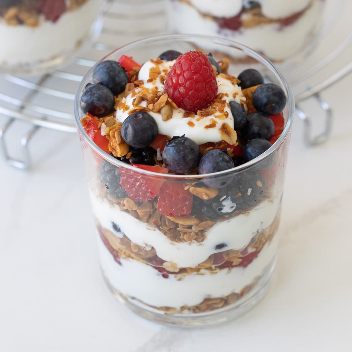 A single yogurt breakfast parfait with layers of fruit, granola, and yogurt in a clear glass.