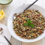 A white bowl of lentil quinoa salad with basil leaves and a serving spoon.