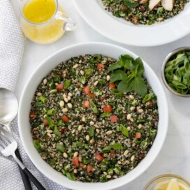 A bowl of tabouli with lots of green parsley, mint, tomatoes, quinoa, and pine nuts.