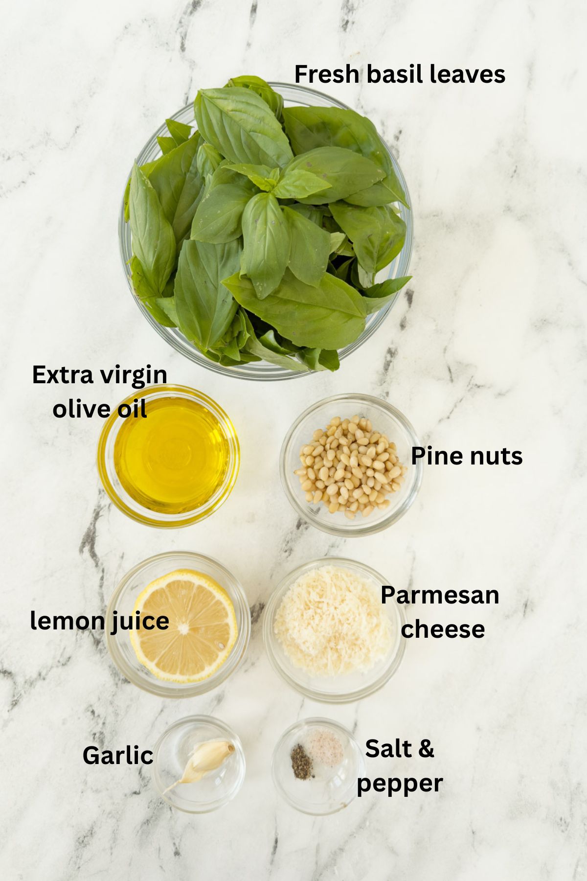 Ingredients for basil pesto (pesto alla Genovese) on a counter in glass prep bowls.