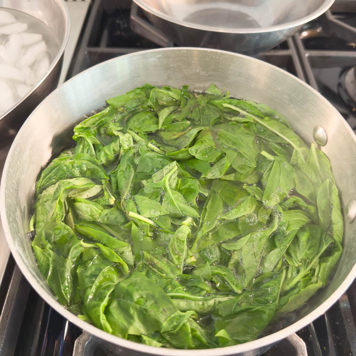 Bright green basil leaves in a pot of boiling water.