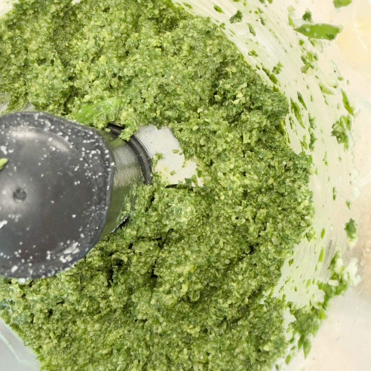 Bright green basil pesto in a food procesor workbowl.