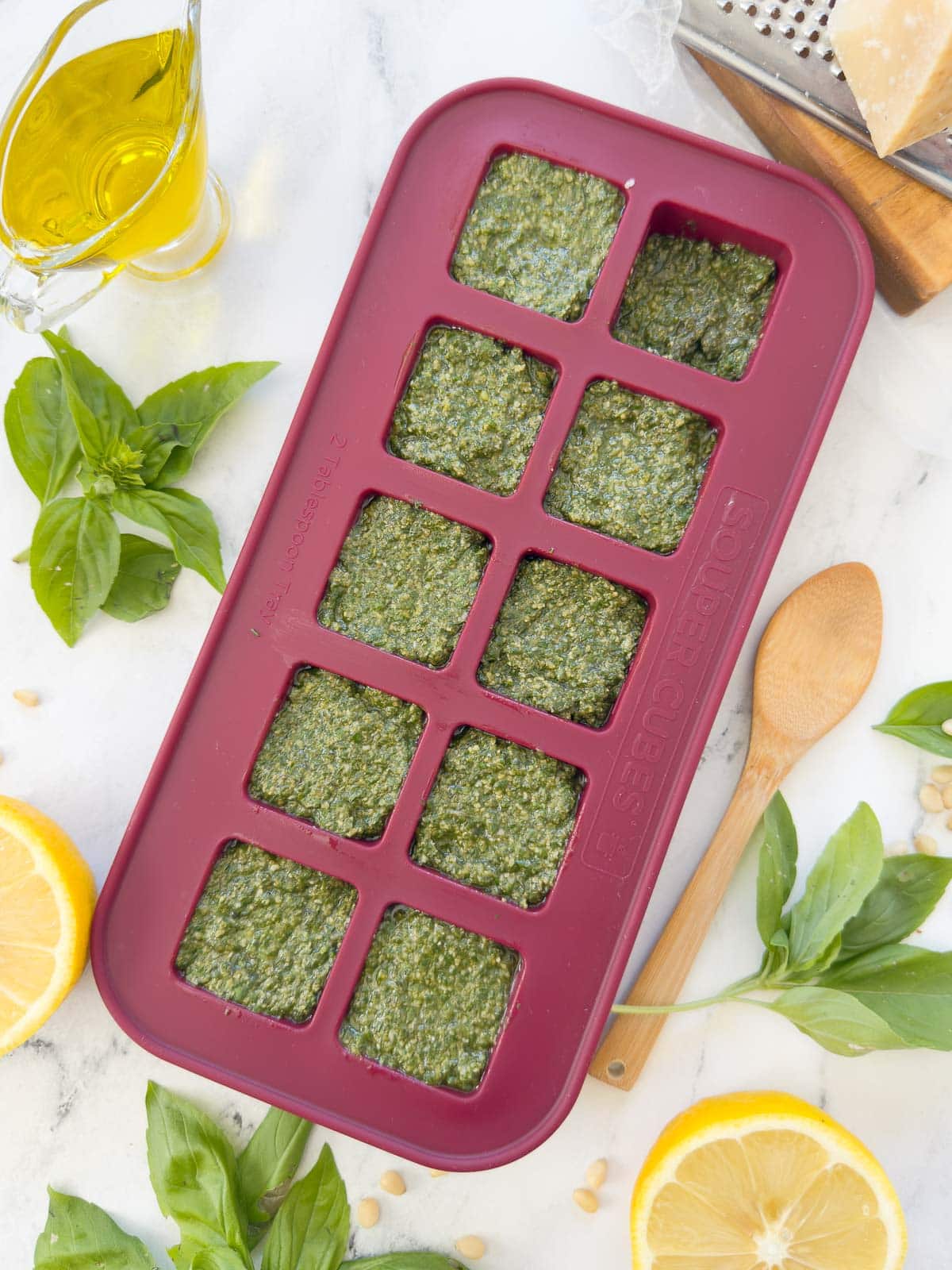 Bright green basil pesto in a cranberry Souper Cubes tray for freezing.