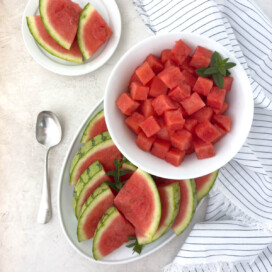 A white platter of watermelon slices and a bowl of cubes.