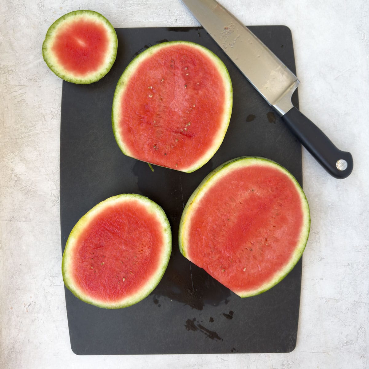 Big slices of red watermelon on a black cutting board with knife.